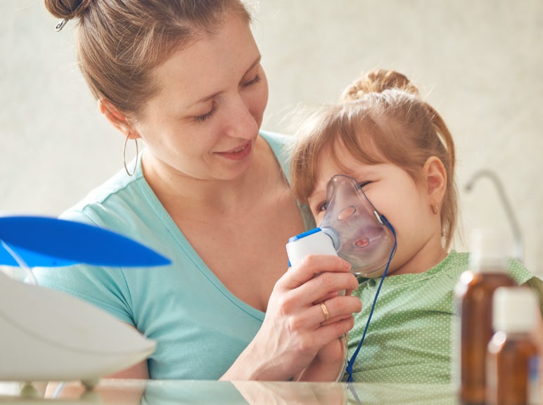 woman makes inhalation to a child at home. brings the nebulizer mask to his face. inhales the vapor of the medication. the girl breathes through the mask. medicine on the table. the care of the mother